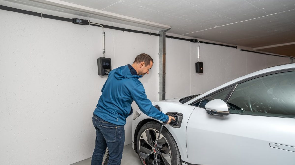 Kapalı garajda elektrikli otomobilini ev tipi şarj ünitesine bağlayan kullanıcı